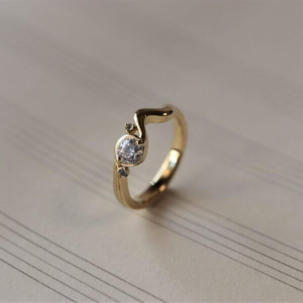 A full-custom engagement ring for a couple who love music. We designed a motif of quarter rests from the arm to the diamond.